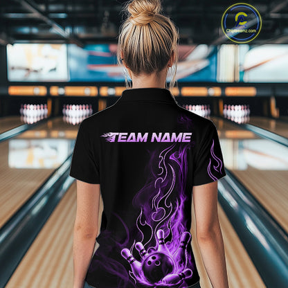 A woman viewed from behind wearing a black short-sleeve polo shirt with a purple and white flame bowling pin graphic and 'TEAM NAME' text on the back, standing in a bowling alley.