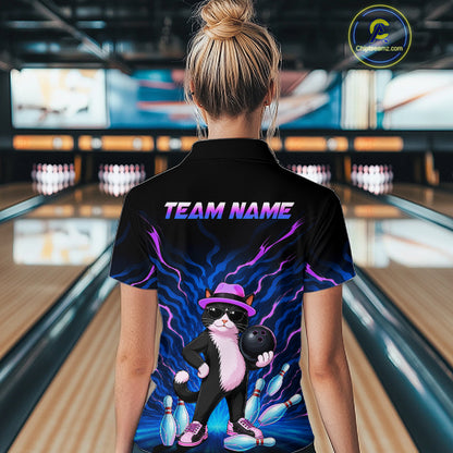 A woman viewed from behind wearing a black short-sleeve bowling-themed polo shirt with a colorful cat graphic and 'TEAM NAME' text, standing in a bowling alley.
