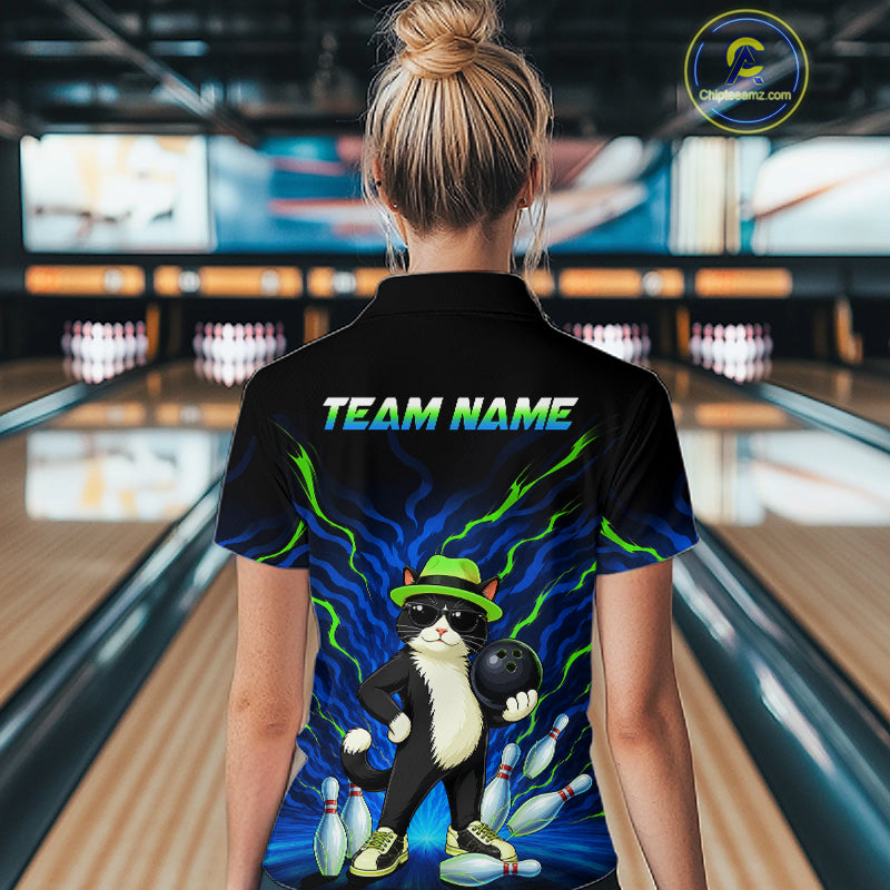 A woman viewed from behind wearing a black short-sleeve bowling shirt with a colorful graphic of a cat bowling and the text 'TEAM NAME' on the back. The background shows blurred bowling alley lanes and pins.