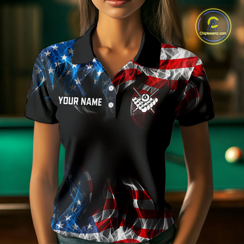 A woman wearing a black short-sleeve polo shirt with a red, white, and blue American flag and stars pattern, featuring a custom name placeholder on the left chest and a billiards-themed crest on the right chest. A green pool table is blurred in the background.