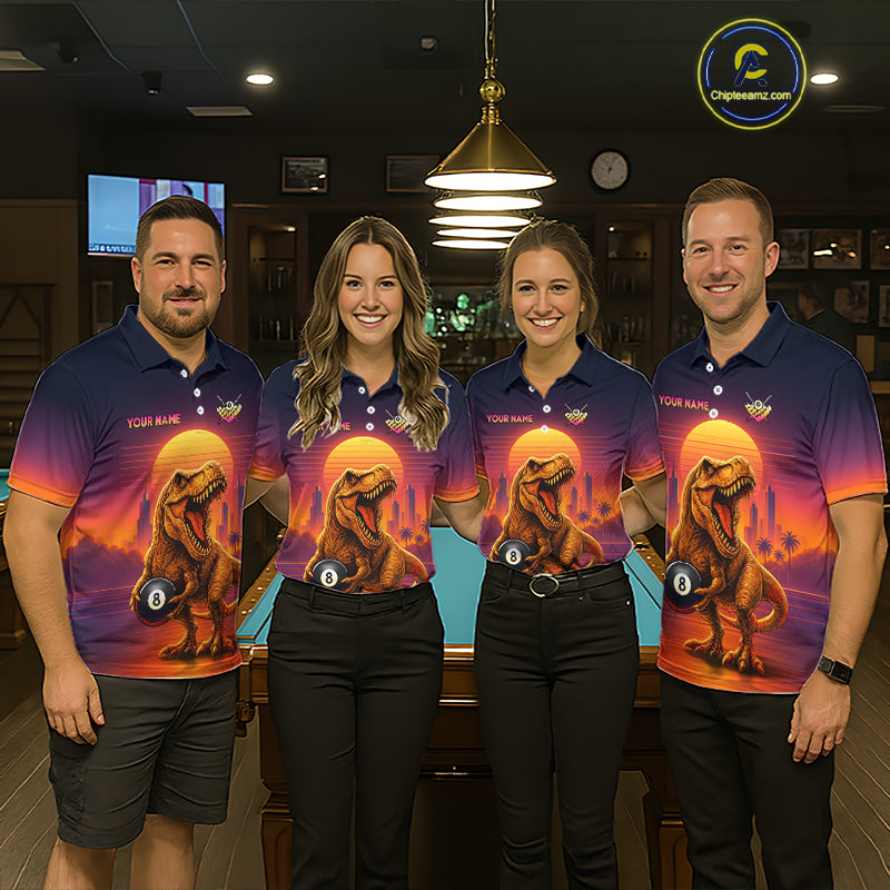 Four people standing indoors wearing matching polo shirts with a colorful dinosaur graphic print. The shirts feature a gradient from dark blue at the top to orange and purple at the bottom, with a large theropod dinosaur and glowing sun design on the front.