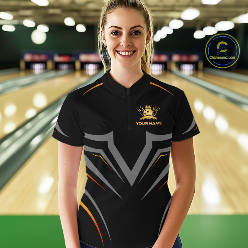 Woman wearing a black bowling shirt with a logo and text in a bowling alley.