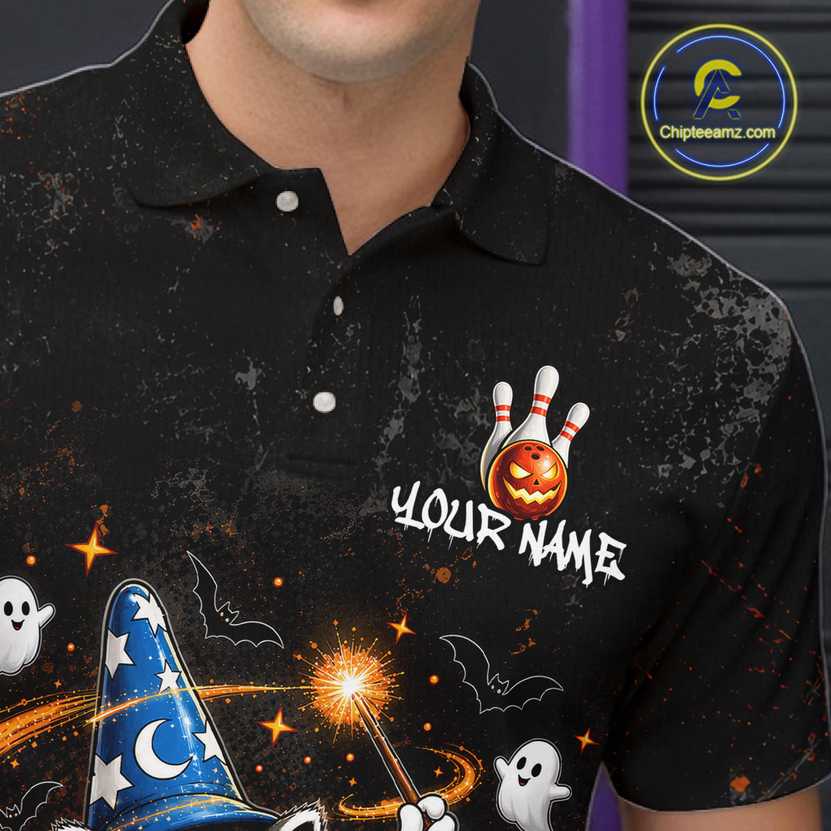A close-up of a person wearing a black short-sleeve polo shirt with a Halloween-themed graphic print. The design features a jack-o'-lantern bowling ball with white bowling pins, the text 'YOUR NAME', white ghosts, a blue wizard hat with stars and a crescent moon, bats, and orange sparkles on a dark background.