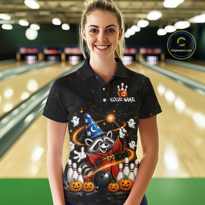A woman stands in a bowling alley wearing a black short-sleeve polo shirt with a large Halloween raccoon graphic on the front. The shirt features a wizard hat, orange pumpkins, ghosts, and white bowling pins, with 'YOUR NAME' printed on the chest.