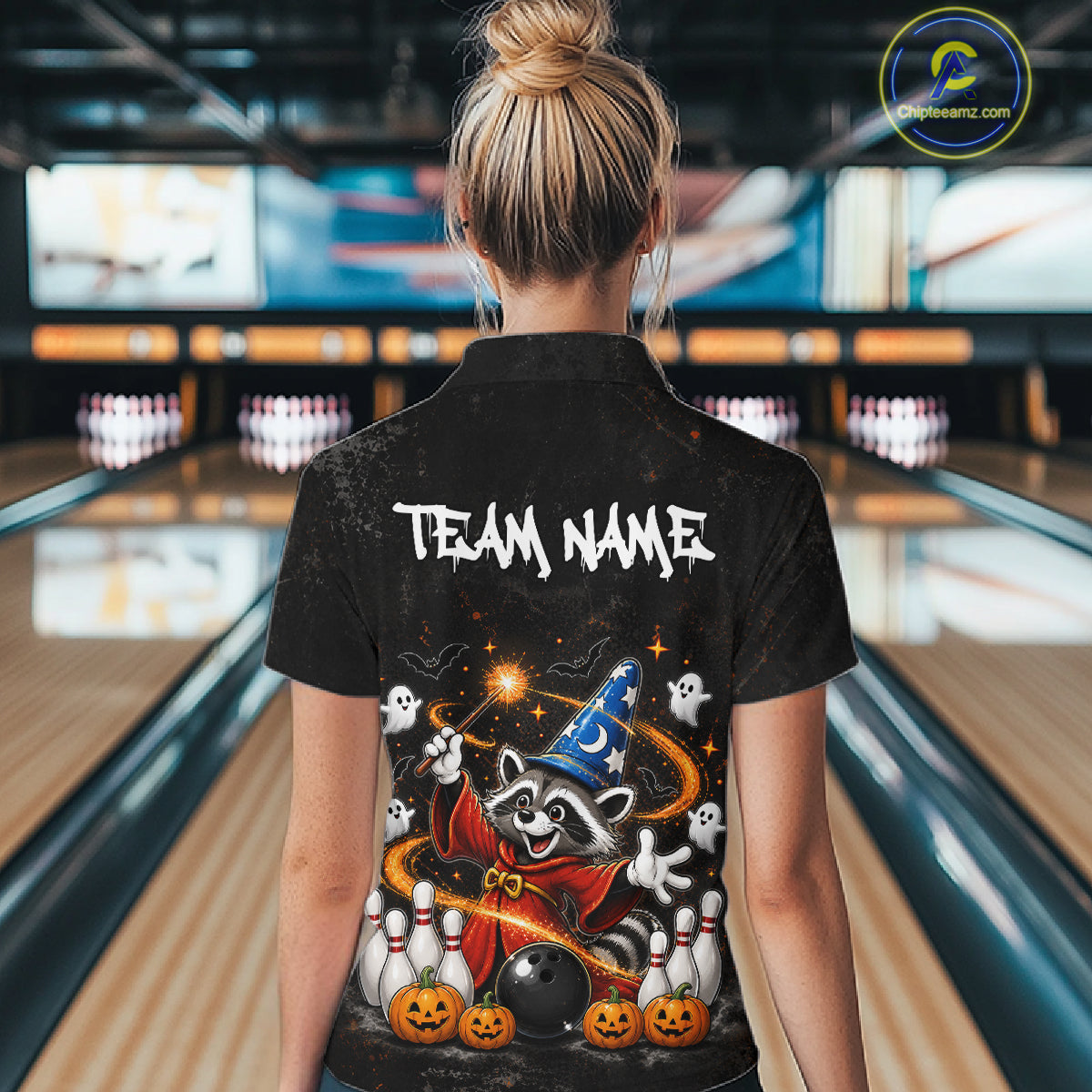 A woman viewed from behind wearing a black short-sleeve collared shirt with a large Halloween-themed graphic on the back. The shirt features the text 'TEAM NAME' in white above a raccoon dressed as a wizard with ghosts, pumpkins, and bowling pins.