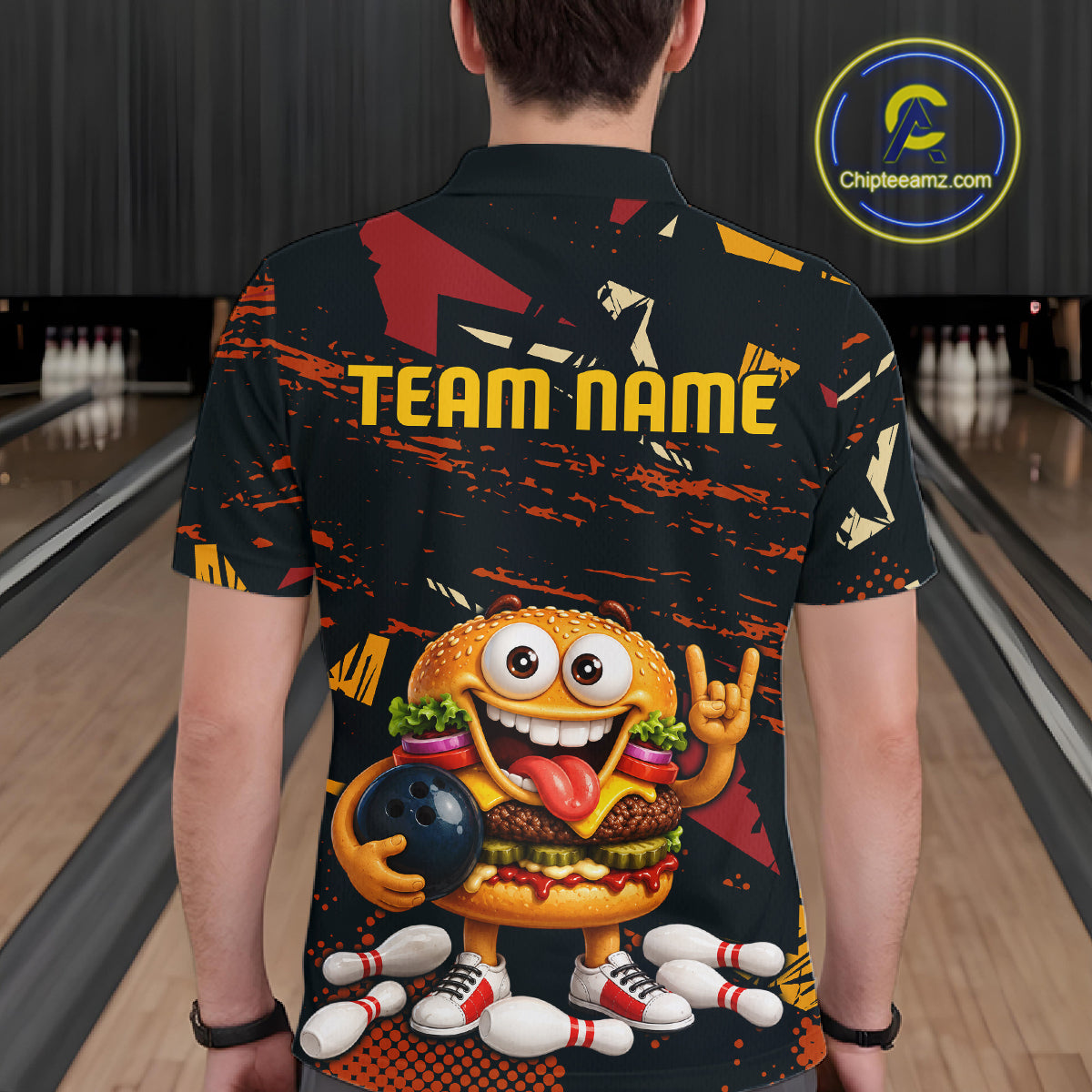 A person viewed from behind wearing a black short-sleeve bowling-themed t-shirt with a large cartoon burger graphic, bowling pins, and the text 'TEAM NAME' on the back. The background shows bowling lanes, and a circular 'Chipteeamz.