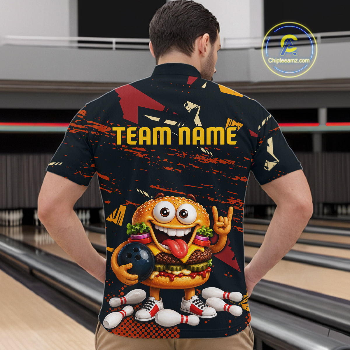 A man viewed from behind wearing a black short-sleeve bowling-themed shirt with a large cartoon burger character, bowling pins, and the text 'TEAM NAME' on the back. Bowling lanes are visible in the background.