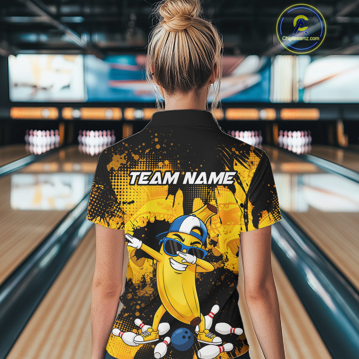 Woman wearing a black and yellow bowling quarter zip featuring a cool banana mascot dabbing, bowling pins, a blue bowling ball, and custom team name text.