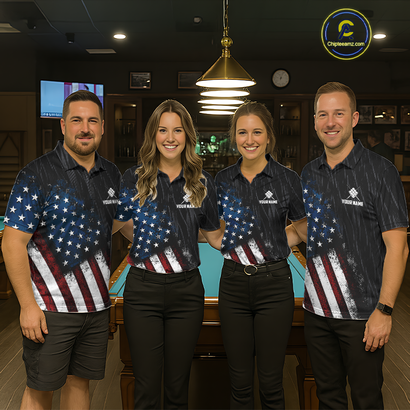 Four people standing together in a dimly lit bar or lounge, wearing matching dark polo shirts with a distressed American flag print on the lower half and a small white chest logo that reads 'CrewWing'. A pool table is visible behind them, along with hanging lights and bar shelving.
