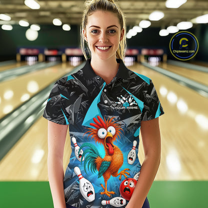 A woman standing in a bowling alley wearing a custom short-sleeve bowling shirt with a colorful cartoon rooster and bowling pins graphic. The shirt features a black and teal patterned upper section and a vibrant blue lower section with a cartoon rooster and bowling pins.