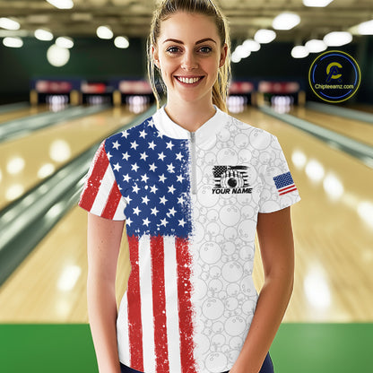 A woman stands in a bowling alley wearing a short-sleeve bowling shirt with a split American flag design: one half shows a distressed red, white, and blue flag pattern, and the other half is white with faint bowling ball graphics and a black chest graphic. 
