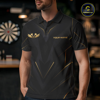 A man wearing a black short-sleeve polo shirt with gold geometric line patterns, a gold winged logo on the left chest, and 'YOUR NAME' printed on the right chest. The background is a blurred bar or sports room setting with a dartboard visible.