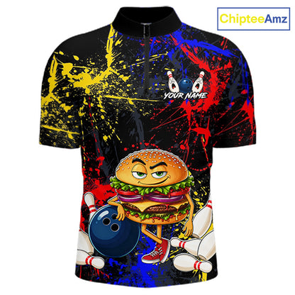 A short-sleeve black quarter-zip bowling shirt with a colorful all-over graphic print featuring a cartoon burger holding a bowling ball, bowling pins, and paint splatters in yellow, red, and blue. The shirt has a mock neck and a 'YOUR NAME' customization placeholder on the chest.
