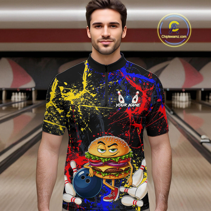 A man wearing a short-sleeve black bowling-themed t-shirt with a colorful paint splatter design and a cartoon burger character holding a bowling ball. The background shows a blurred bowling alley.