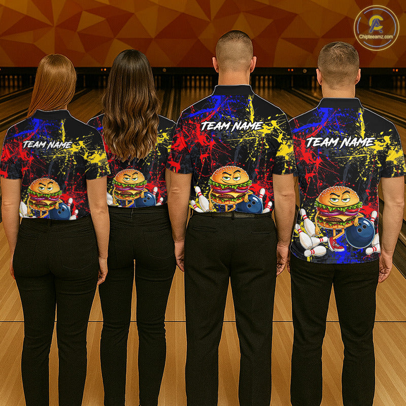 Four people standing from the back in a bowling alley, wearing matching black short-sleeve bowling shirts with colorful paint-splatter graphics, cartoon burger characters, bowling pins, and bowling balls, plus customizable 'TEAM NAME' text on the upper back.