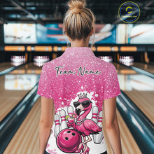 Load image into Gallery viewer, Back view of a female model in a bowling alley wearing a pink polo shirt featuring a crowned flamingo holding a cocktail beside a bowling ball.