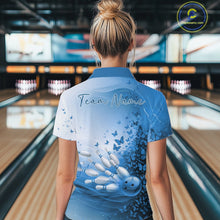 Load image into Gallery viewer, Back view of a white and blue women s bowling polo shirt showcasing butterfly artwork and bowling-themed graphics inside a bowling center.