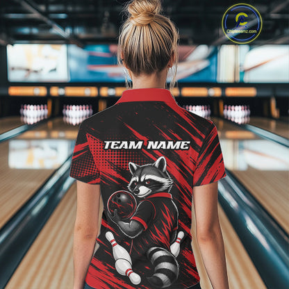 A woman viewed from behind wearing a short-sleeve bowling polo shirt with a raccoon graphic and 'TEAM NAME' text on the back, standing in a bowling alley.