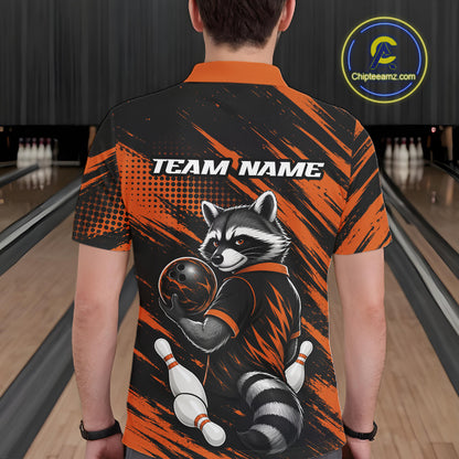 A person viewed from behind wearing a short-sleeve collared shirt in a bowling alley. The shirt has an orange and black brush-stroke design with a raccoon holding a bowling ball and pins, and the text 'TEAM NAME' across the upper back.