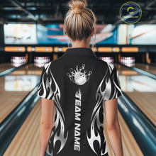 Load image into Gallery viewer, Female model back view at a bowling lane wearing a black polo shirt featuring a silver metal tribal flame design with a bowling ball striking pins in dynamic motion.