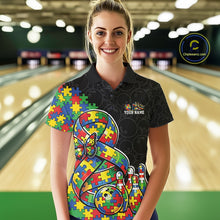 Load image into Gallery viewer, Female model in a bowling lane wearing a black polo shirt, front view showing a large autism awareness ribbon filled with puzzle pattern, colorful butterfly, and bowling ball striking pins artwork