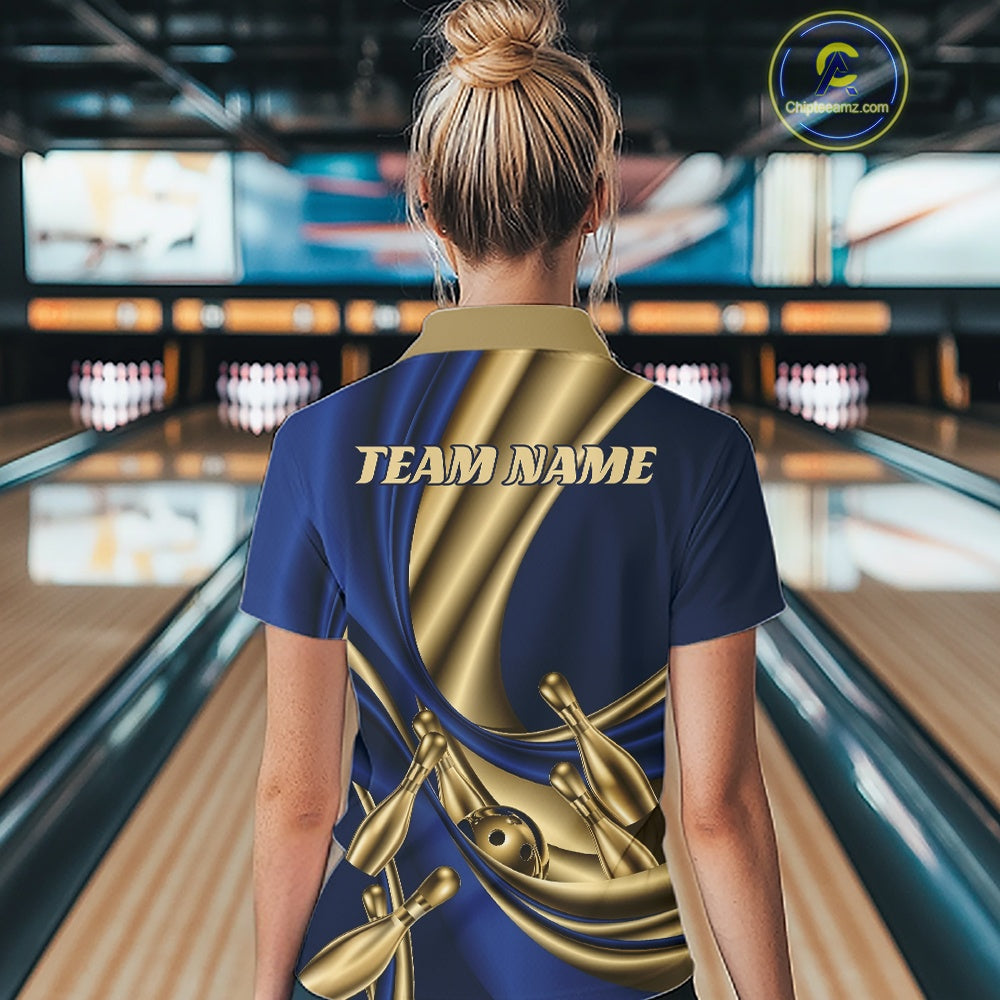 A woman viewed from behind wearing a custom bowling-themed polo shirt with a navy blue and metallic gold design featuring bowling pins and the text 'TEAM NAME'. The background shows a blurred bowling alley with lanes and pins.