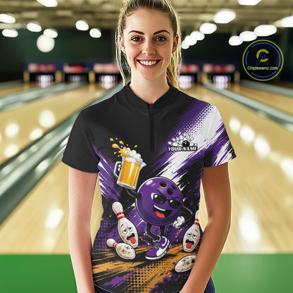 A woman stands in a bowling alley wearing a black and purple short-sleeve bowling quarter zip  with a cartoon bowling ball character, bowling pins, and a beer mug graphic. 