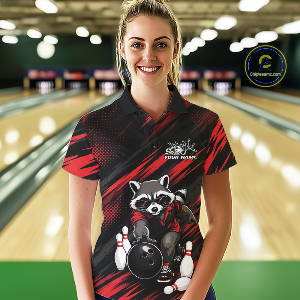 A woman stands in a bowling alley wearing a custom short-sleeve polo shirt with a raccoon bowling graphic and red and black diagonal stripes. The background shows blurred bowling lanes.