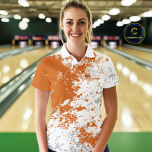 Load image into Gallery viewer, Female model front view at bowling lane wearing white polo shirt with orange and white splatter design, casual bowling alley environment