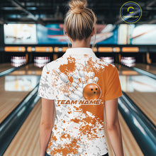 Load image into Gallery viewer, Back view female model in bowling venue wearing white polo with orange and white splatter pattern, standing near bowling lane