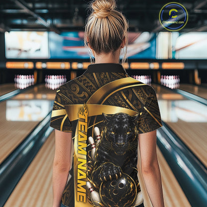A woman viewed from behind wearing a short-sleeve bowling shirt with a black and gold graphic design featuring a panther and the text 'TEAM NAME'. The background shows a blurred bowling alley with lanes and pins.