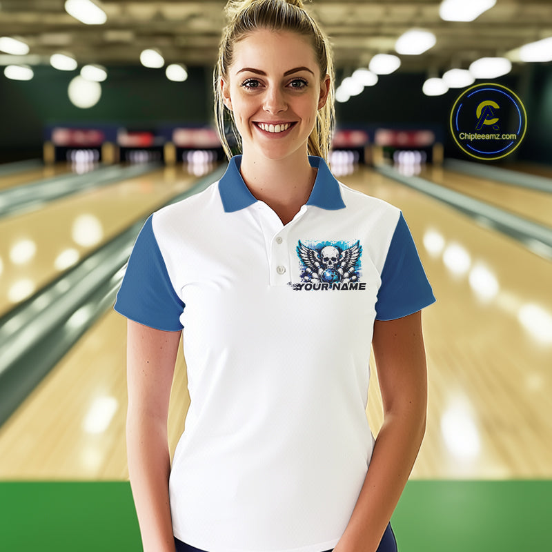 A woman stands in a bowling alley wearing a bowling shirt with polo collar, blue skull-themed bowling graphic with black wings, pins, bowling ball