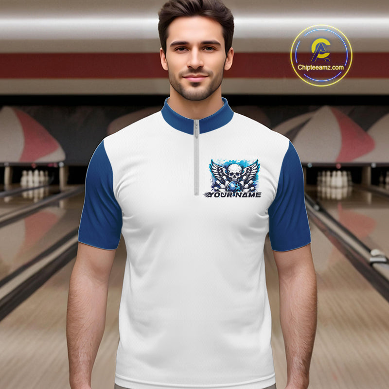 A man stands in a bowling alley wearing a bowling shirt with quarter zip collar, blue skull-themed bowling graphic with black wings, pins, bowling ball