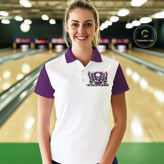 A woman stands in a bowling alley wearing a bowling shirt with polo collar, purple skull-themed bowling graphic with black wings, pins, bowling ball
