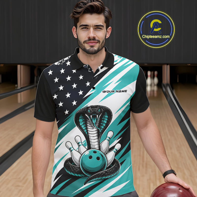 A smiling man stands in a bowling alley wearing a black, white, and blue bowling shirt with stars, diagonal stripes, a cobra, pins, and an blue ball.