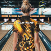 Load image into Gallery viewer, Back view of a female model wearing a bowling quarter zip shirt featuring a black and gold bowling ball hitting the pins graphic with flowing metallic ribbon accents at a bowling lane.