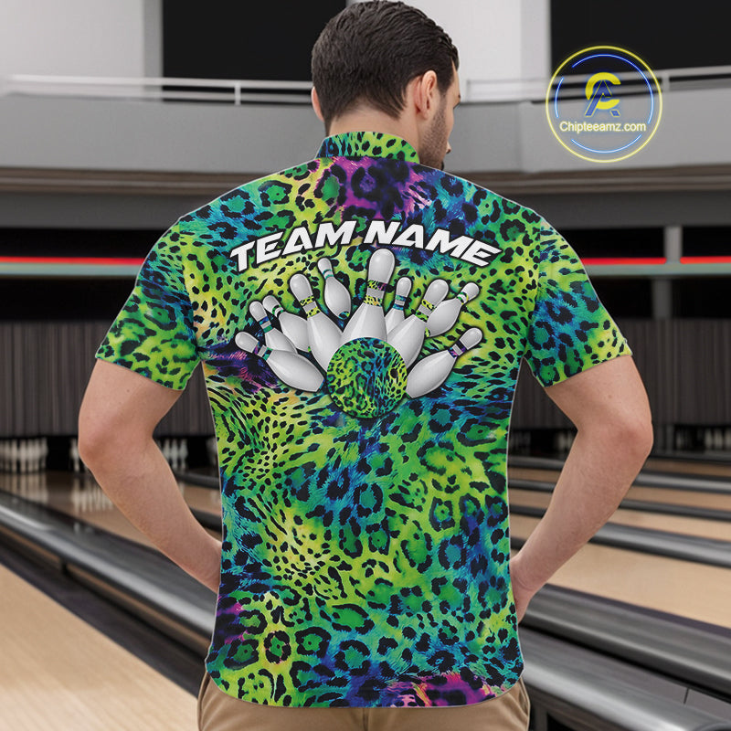 Back view of a man standing at a bowling alley, wearing a blue, green, and black leopard-print bowling polo with “Team Name” and bowling pins on the back.
