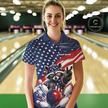 Load image into Gallery viewer, Female model wearing a bowling polo shirt featuring a patriotic raccoon flashing a peace sign, a red, white, and blue bowling ball hitting the pins, and a flowing American flag, shown from the front in a bowling lane.