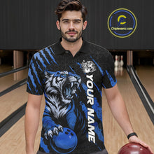 Load image into Gallery viewer, Front view of a male model wearing a black and mid blue bowling polo shirt at a bowling lane, showcasing a roaring tiger holding a mid blue bowling ball with matching claw-stripe artwork and a geometric background pattern.
