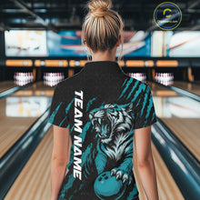 Load image into Gallery viewer, Back view of a female model in a bowling lane wearing a black and teal blue bowling polo shirt featuring a roaring tiger holding a teal blue bowling ball with teal blue claw-stripe artwork and a geometric background pattern.