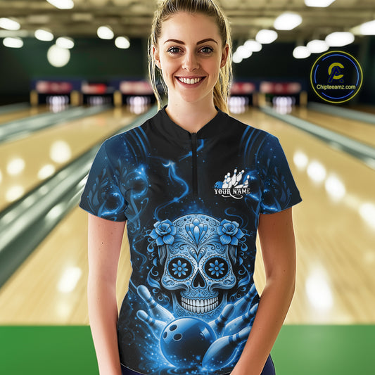 Female model at a bowling lane wearing a black and blue bowling quarter-zip shirt with floral sugar skull artwork and bowling-inspired graphics.