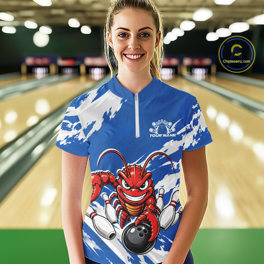 Front view of a happy female model in a bowling alley wearing a blue custom quarter zip bowling shirt with an aggressive crawfish bowling design and a distressed background.