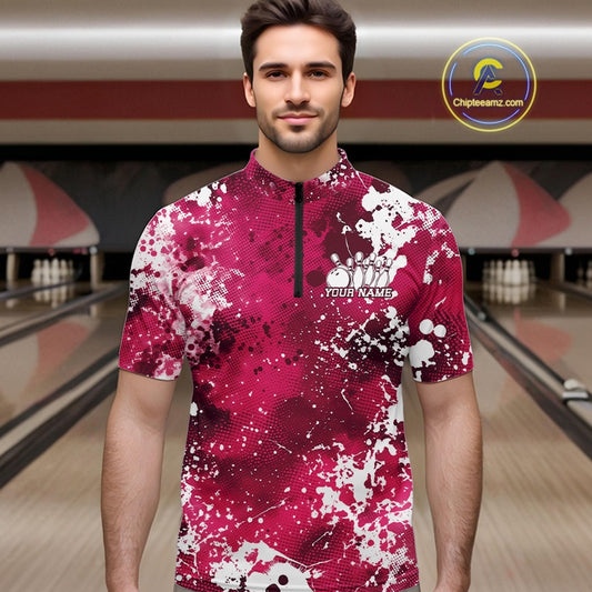 Front view of a male model in a bowling alley wearing a bowling polo shirt featuring a white paint splatter design on a pink shirt.
