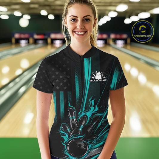 Female model wearing a black and turquoise blue bowling quarter-zip shirt at a bowling lane with patriotic bowling strike graphics and bold flag accents.