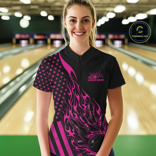Female model wearing a black bowling quarter-zip shirt at a bowling lane with a pink flaming bowling ball knocking down pins and patriotic graphics.