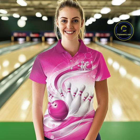 Female model standing in a bowling lane wearing a white and pink bowling polo shirt featuring abstract wave lines and a glossy bowling ball striking pins on the front.