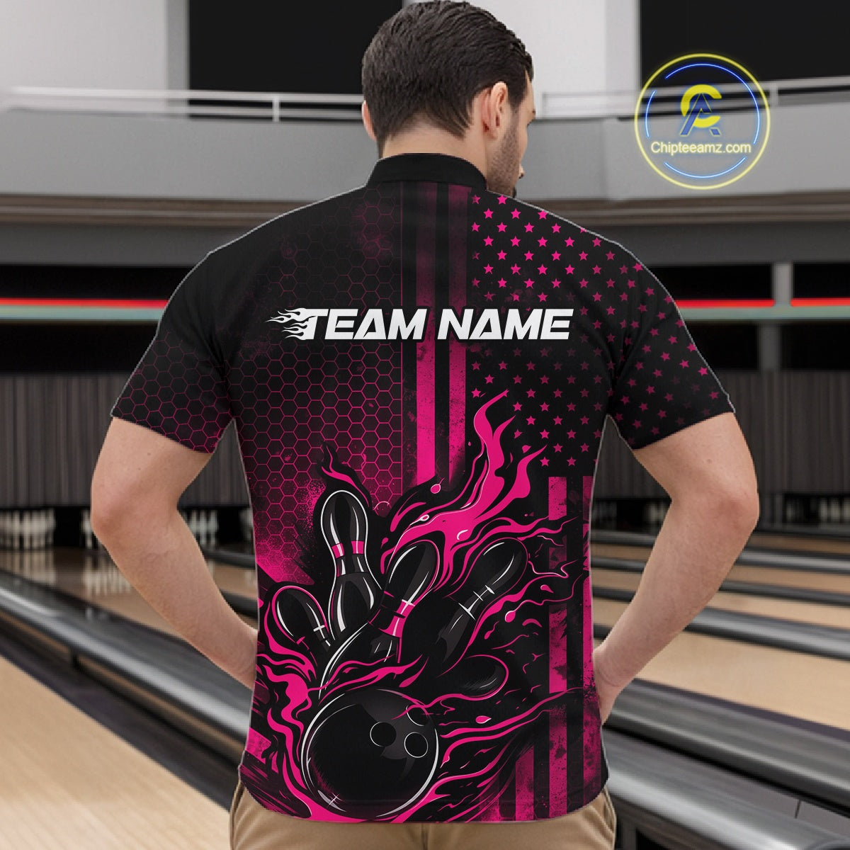 Front view of a male model in a bowling alley wearing a black and pink quarter-zip shirt showcasing a flaming bowling ball hitting the pins.