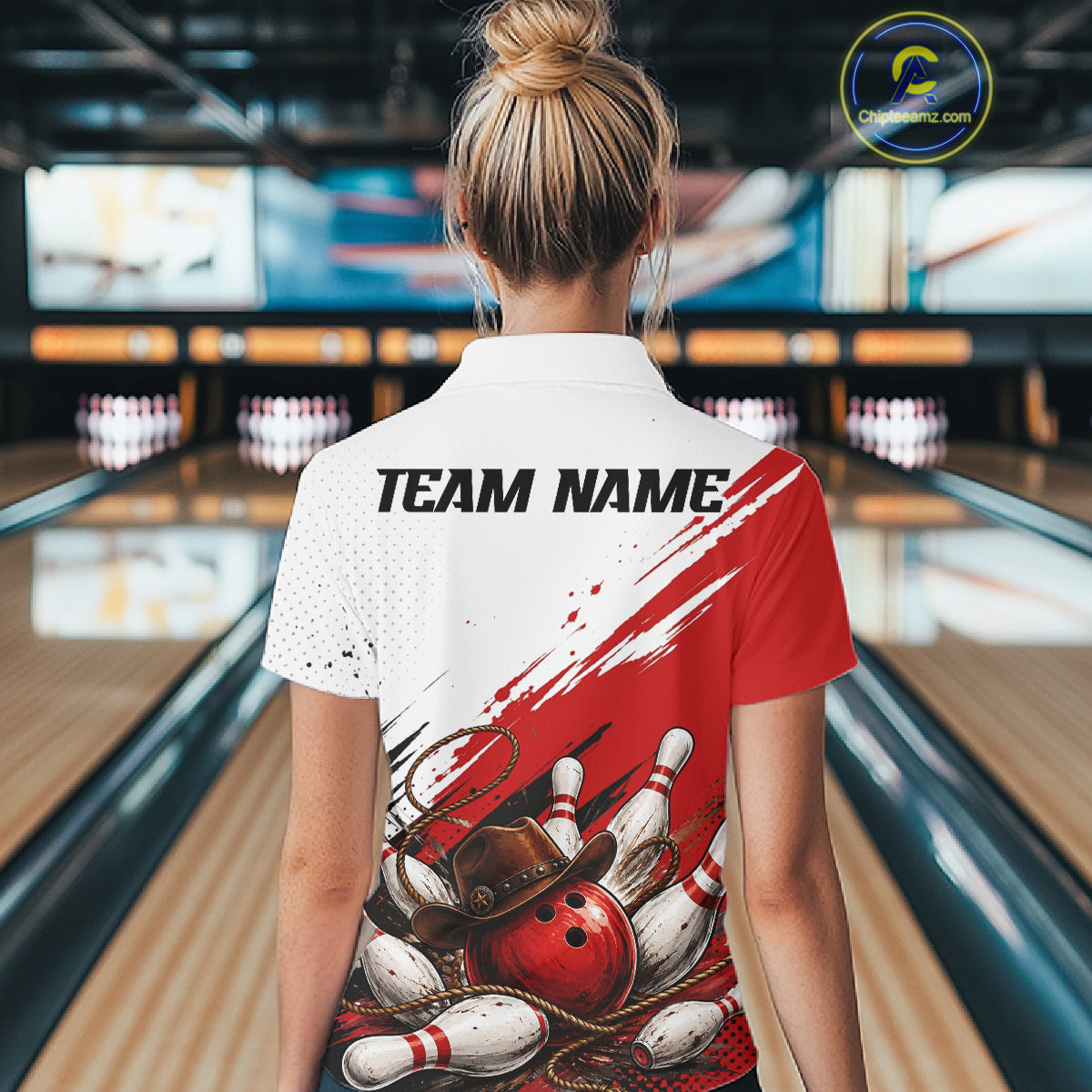 A woman stands in a bowling alley wearing a custom short-sleeve polo shirt with a red and white graphic design featuring bowling pins, bowling balls, and a bowler's hat. The shirt has a white upper chest and shoulder area with red paint-like brushstrokes, a black and white bowling pin graphic, and a red bowling ball with a brown hat.