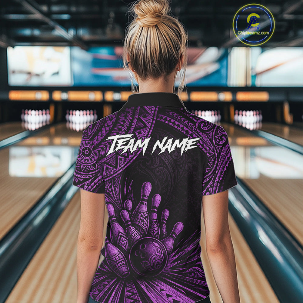 A woman viewed from behind wearing a black short-sleeve bowling shirt with a purple tribal-style hand and bowling ball graphic and the text 'TEAM NAME' across the upper back. Bowling lanes are visible in the blurred background.