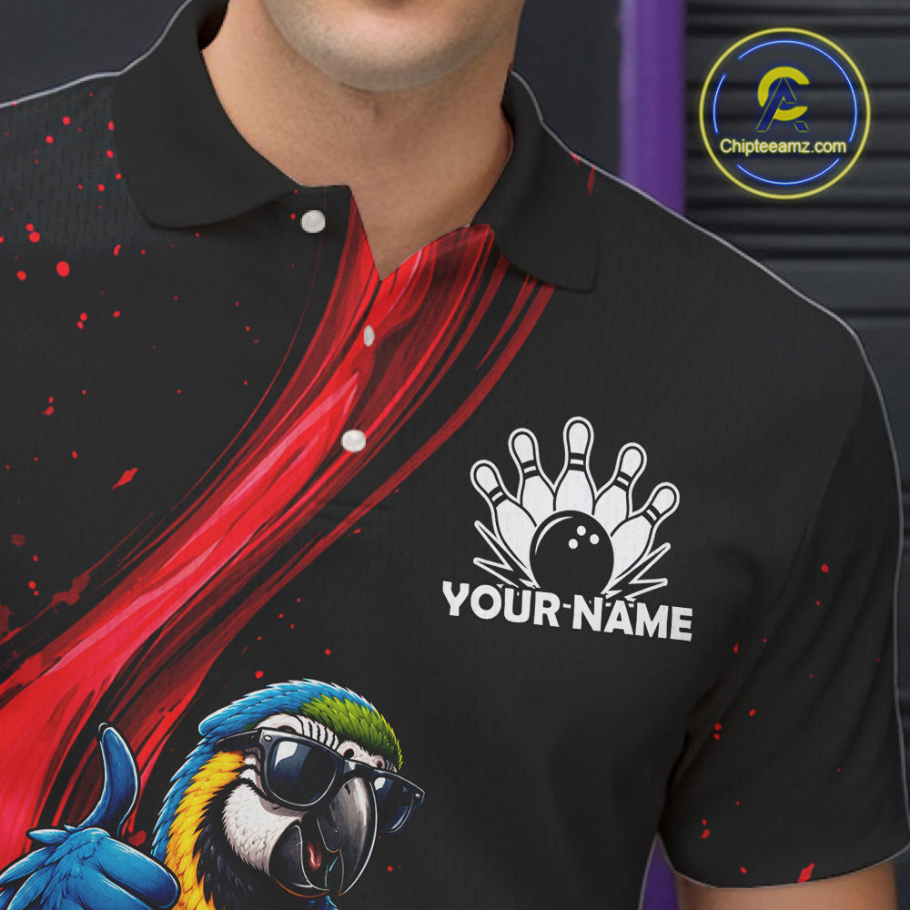 A close-up of a black short-sleeve polo shirt worn by a model, featuring a red abstract graphic on the chest, a white bowling pin and ball graphic with the text 'YOUR NAME', and a colorful parrot illustration in the lower left. A circular 'Chipteeamz.